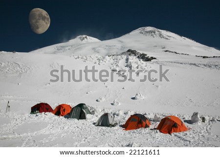 Several tents in the camp on the mountain at night with big moon