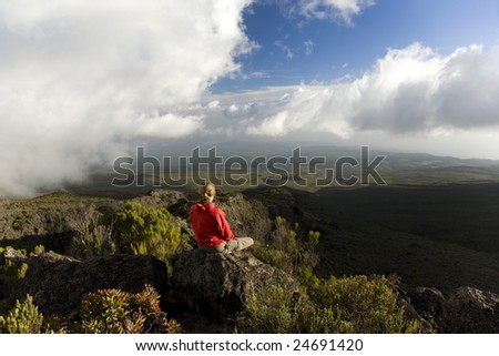 Rear view of woman meditating at the rock of the mountain, looking at view,Mount Kilimanjaro, Africa.Copy space