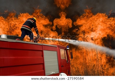 Firefighter on a firetruck, sitting on a fire hose spraying water at a large blaze.