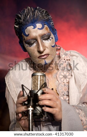 Woman sings with a old microphone, the stage lights. Face Paint.