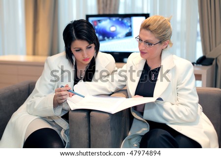 Two young business women at work. Authentic offices and less light, the reason for the presentation of the screen (better visibility) and a business report.