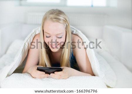 A young woman lying on front in the bed and using smart phone.
