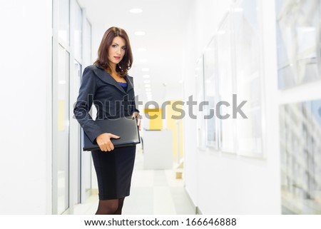 Full length portrait of serious young female professional standing with a folder in office lobby
