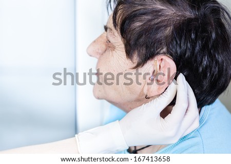 Female doctor putting a hearing aid in a senior women\'s ear