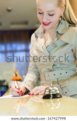 Attractive young women is checked out of the hotel and signs a hotel bill.copy space