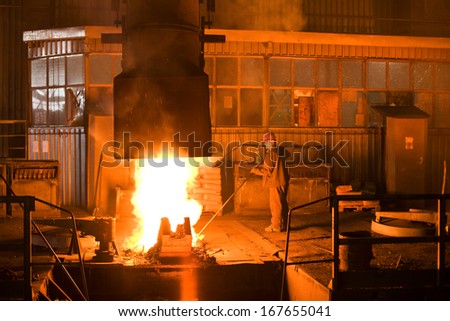 Working in a foundry. Workers looking down, red color is a reflection of the molten metal. Very high heat and purple fringing. See more images and video from this series.