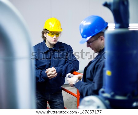 Two workers talking about a job in a factory, controls the operation of devices in a power plant. Shallow Doff. Authentic fluorescent light.