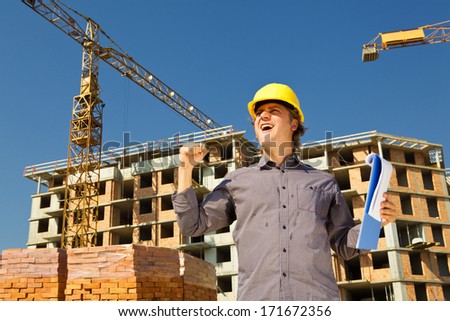 Happy construction architect in a front of a construction site with the cranes.