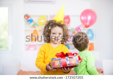 Children having fun at a birthday party. Child standing in front holding birthday presents.