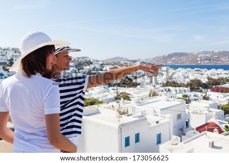 Happy  women standing  on the promenade and looking away, pointing at beautiful cityscape of Mykonos .Copy space