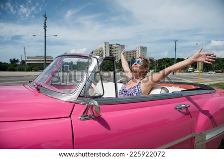 Happy, excited woman with arms outstretched in a pink cabriolet, convertible car