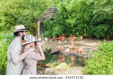 Side view of young, excited couple with binocular watching at pink flamingos.Copy space