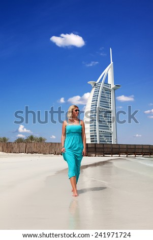 Blonde woman walking along the beach in the front of the Burj Al Arab hotel in Dubai