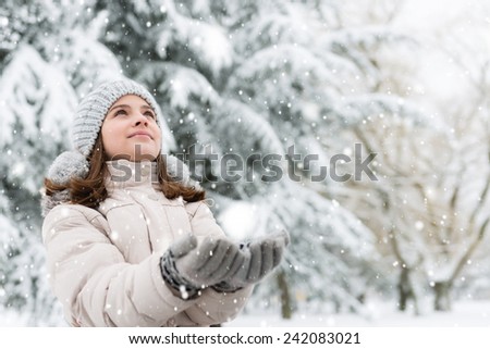 Cheerful, teenage girl looking in the sky, catching a snowflakes.Copy space
