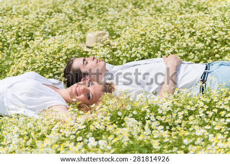 Happy, young couple lying on back in a chamomile, daisy meadow