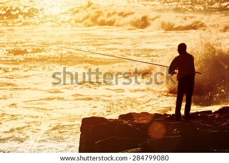 Silhouette of  fisherman fishing on an ocean coast. Unrecognizable person, lens flare, sunset light .Copy space