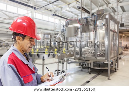 Industrial worker writes on a paper conditions in a filling line production of liquid detergent.Shallow doff