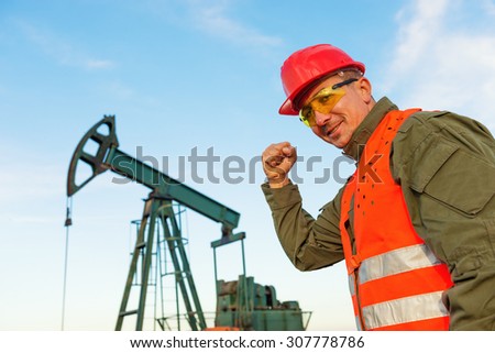 Happy engineer in front of the pump jack say ,,Yes,,looking in camera.Shallow doff