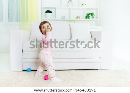 Sweet baby little girl standing in front of the sofa, holding baby toy.Living room interior.Shallow doff, copy space