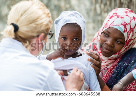 Female Caucasian doctor listening heart beat and breathing of little African girl with stethoscope.Mother holding the child