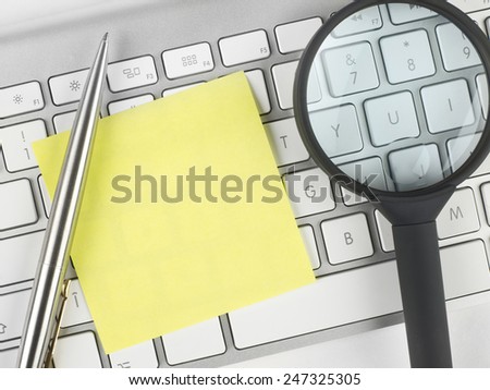 Adhesive note, magnifying glass and pen on keyboard