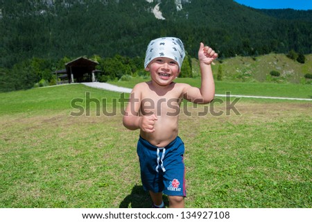 Smiling and happy child, races on the lawn and holds the lifted thumb