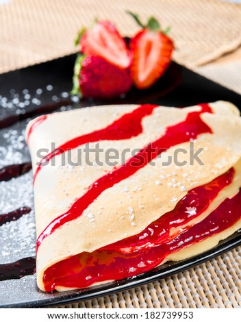 crepes to the strawberry put on a black plate with icing sugar and topping to the strawberry, on the background fresh strawberries