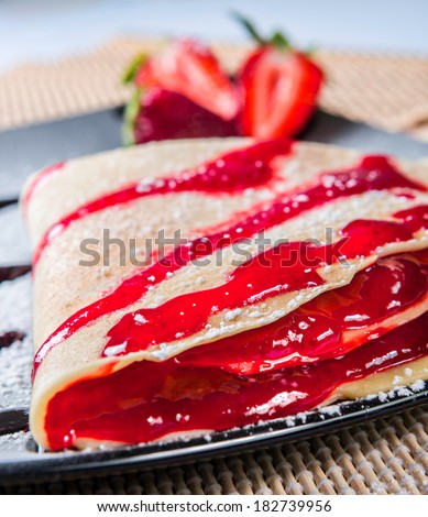 crepes to the strawberry put on a black plate with icing sugar and topping to the strawberry, on the background fresh strawberries