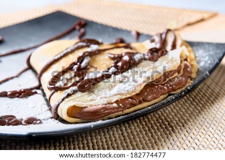 crepes to the chocolate put on a black plate with icing sugar and topping to the chocolate