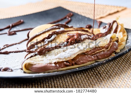 crepes to the chocolate put on a black plate with icing sugar and topping to the chocolate