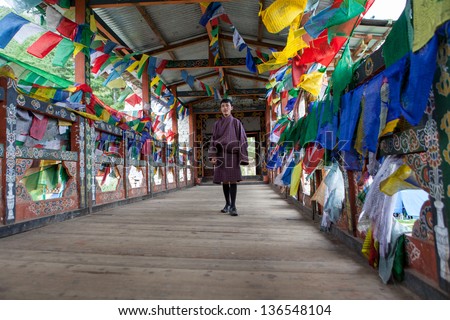 THIMPHU,BHUTAN - SEPTEMBER 22:Bhutanese man in traditional dress surrounded by prayer flags poses on bridge over Wang Cchu river on September 22,2012 in Thimphu,Bhutan.