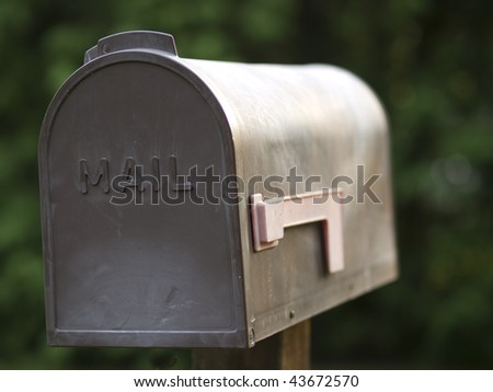 Brown plastic mailbox with a red flag outdoors against a green background.