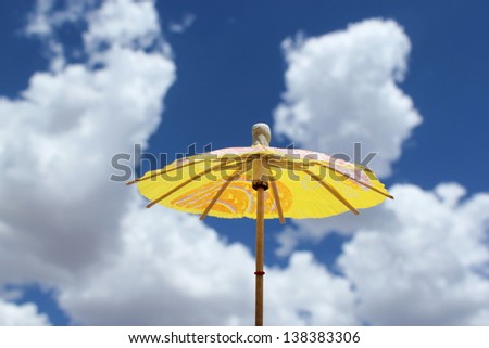 Yellow cocktail umbrella with blue sky and clouds