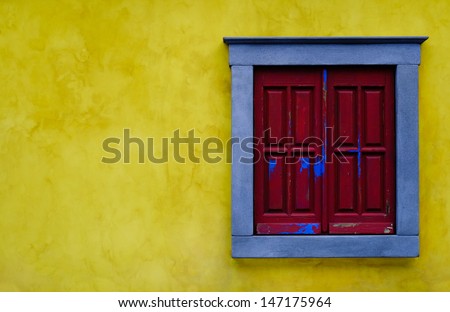 Closed red window shutters with a blue frame on a yellow brick wall