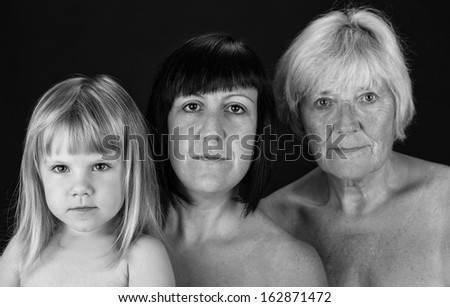 Three generations of women from the same family looking at the camera in black and white. Studio shot on a black background.