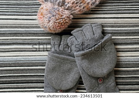 Woolen hat wit pompom and gloves on a striped knitting background