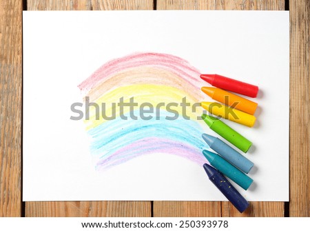 Crayons lying on a paper with children\'s drawing rainbow. Selective focus, copy space background, top view