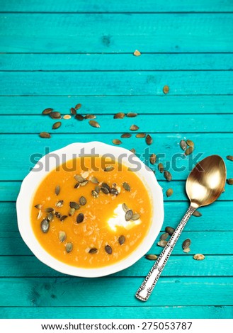 Still life, food and drink concept. Pumpkin soup with sour cream and seeds on a wooden turquoise table. Selective focus, copy space background, top view