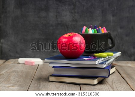 Still life, business, education concept. Crayons (pencils) in a mug, notebooks and apple on a wooden table with chalkboard. Selective focus, copy space, school background