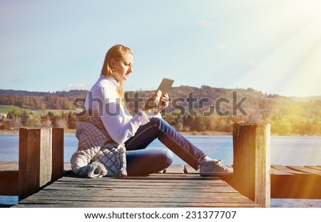 Girl reading from a tablet on the wooden jetty against a lake. Switzerland