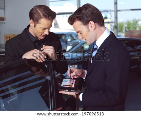 Man buying a car, the salesman talking to him and explaining details on laptop
