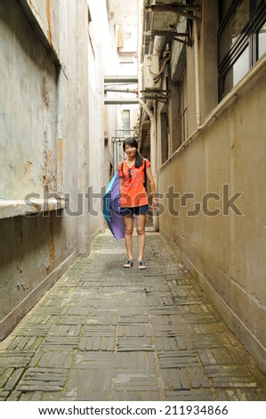 A Chinese woman walking down a narrow alley way with an umbrella in an old converted factory.