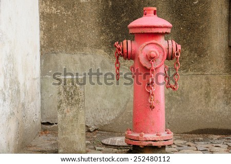 A weathered red fire hydrant near a cement wall.