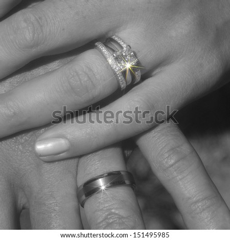 Bride and groom\'s wedding bands on their hands in black and white, with spot color on the diamond sparkle