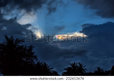 Sundog in the sky as storm clouds move in, just above the palm trees, as the sun is about to set