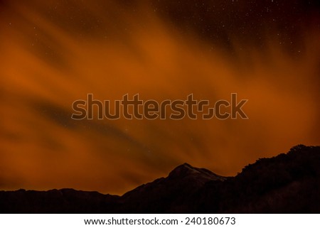 Red clouds reflecting the nearby radio tower lights moving past the mountain top during a starry night long exposure