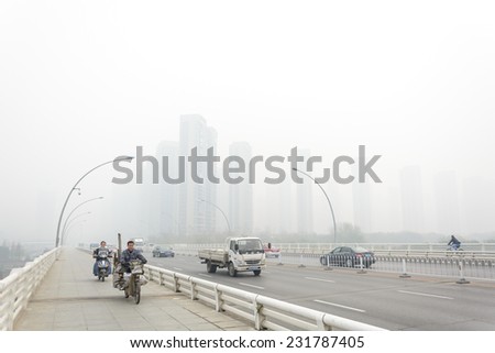 SHENYANG, CHINA - OCTOBER 31, 2014: City in a heavy hazy weather, people are riding electric bicycle. Located in Sanhao Bridge, Shenyang City, Liaoning Province, China.