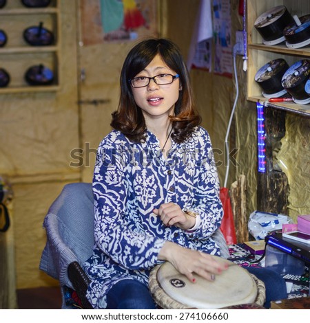 Lijiang, China - April  4, 2014: Chinese girl playing djembe in a music store. Located in Old Town of Lijiang, Yunnan Province, China.
