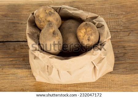 Paper bag of unwashed potatoes on a brown oak board
