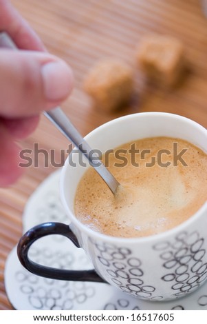 Hand holding a spoon in a cup of coffee with brown sugar in the background